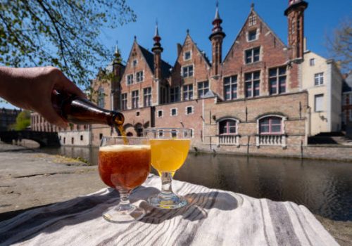 Tasting of Belgian beer on open cafe or bistro terrace with view on medieval houses and canals in Bruges, Belgium in sunny day